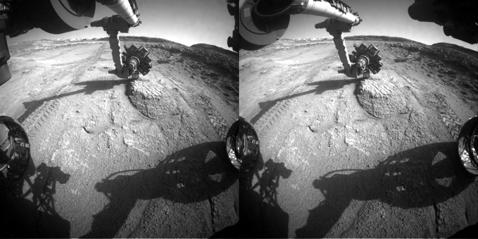 A dual left/right stereoscopic pair of black and white photographies capturing the Mars rover Curiosity robotic arm, instrumented turret, front wheels, with the right wheel projecting its shadow on the foreground. This dual image is intended to be used to obtain a Stereo3D rendition of the scene through parallel viewing, and not cross-eyed viewing.
