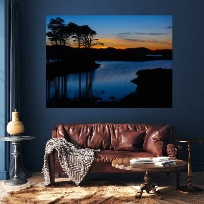 An advert picture featuring a sunset wall art with dark blue reflections on the water of a Highland Loch the trees are silhouetted against the warm glowing sky on the horizon 