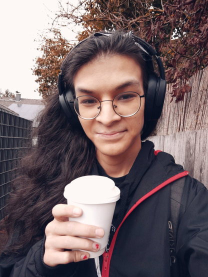 Happy selfie with long hair open and a hairband with a black/white striped bow. Wearing headphones, glasses and a coffee to-go in one hand.